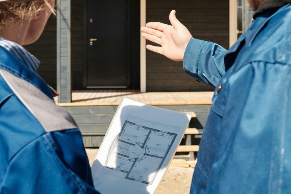 Une femme, tenant les plans d'une maison, et un homme, montrant le porche d'une maison, de dos.